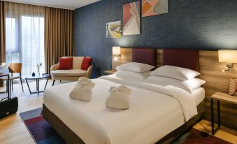a large bed with white linens and a headboard is in a room with blue walls at Mercure Geneva Airport