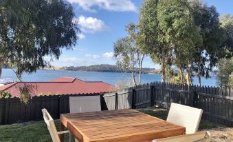 a wooden table and chairs are set up in a backyard with a view of the water at Eastcoaster Tasmania