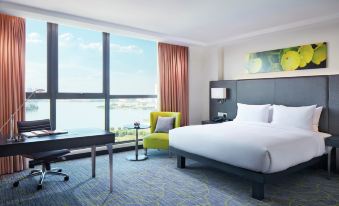 a modern hotel room with a large window overlooking the ocean , featuring a comfortable bed , desk , and chair at Hilton Garden Inn Puchong