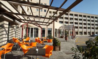 an outdoor dining area with orange chairs and tables under a wooden pergola , overlooking a building at Travelodge Barcelona del Valles