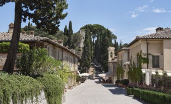 a cobblestone street in an old town , surrounded by buildings and trees , with a church visible in the background at Rosewood Castiglion del Bosco