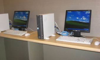 two computer monitors are placed on a desk with two keyboards and a desktop computer at Meitetsu Inn Kariya