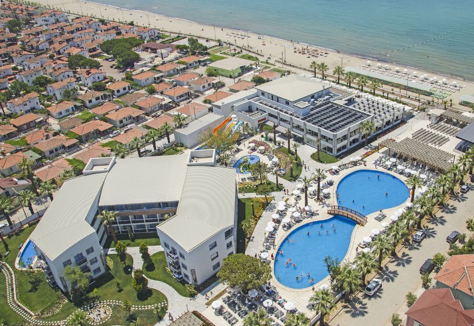 aerial view of a large resort with multiple buildings , swimming pools , and a beach in the background at Palm Wings Kusadasi Beach Resort&Spa