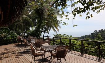 a wooden deck with several chairs and tables , overlooking a beautiful view of the ocean at Lapa Rios Lodge by Boena