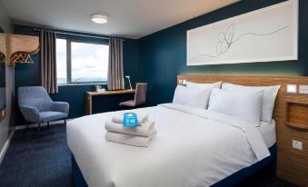 a modern hotel room with a large bed , blue walls , and a painting on the wall at Travelodge Porthmadog