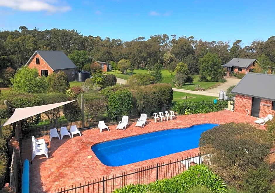 a large pool is surrounded by white lounge chairs and a red brick patio , with a house in the background at Prom Coast Holiday Lodge