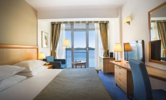 a hotel room with a large window overlooking the ocean , featuring a bed , desk , chair , and tv at Aminess Grand Azur Hotel