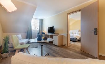 a modern living room with a flat - screen tv , couch , and dining table , as well as a bedroom with a bed at Select Hotel Erlangen