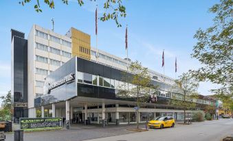 a modern building with a yellow car parked in front and flags on the roof at Best Western Plus Airport Hotel Copenhagen