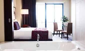 a luxurious hotel room with a large bed , a bathtub , and a view of the city at Rydges Campbelltown an EVT hotel