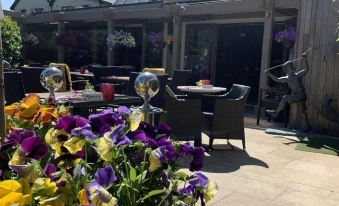 a sunny outdoor terrace with a variety of flowers , including pansies and other plants , surrounded by wooden furniture and a clear blue sky at Horse & Hound