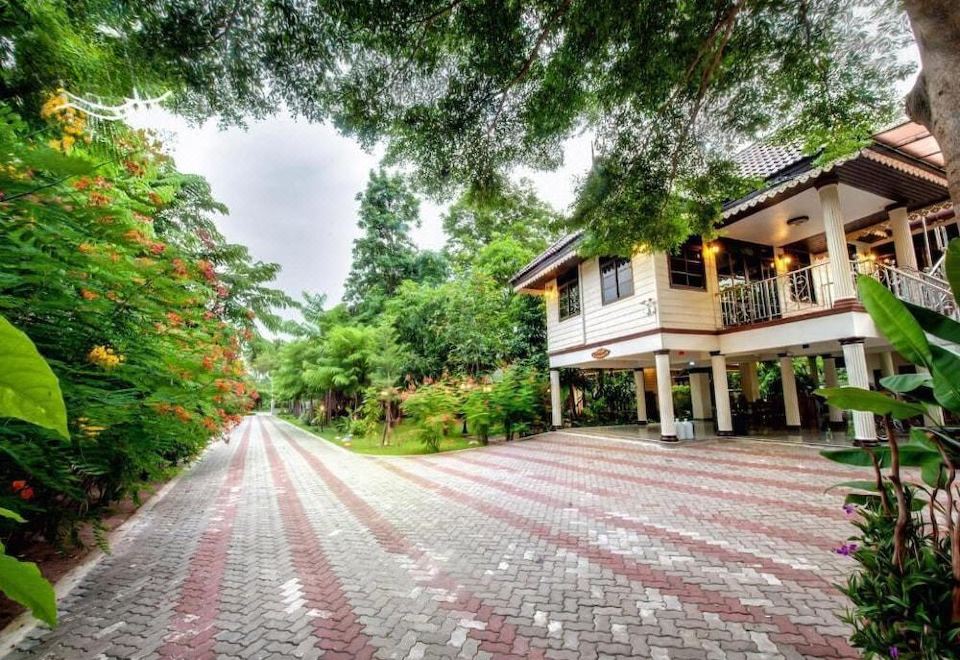 a house is nestled in a tropical setting with trees and a brick path leading up to it at Baan Nam Pen Resort