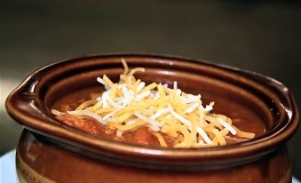 a bowl of chili is filled with ground meat and topped with shredded cheese , sitting on a dining table at Waynebrook Inn