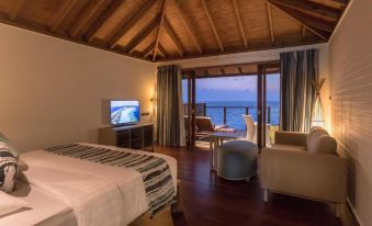 a bedroom with a bed , chair , and television is shown with a view of the ocean at Vilamendhoo Island Resort & Spa