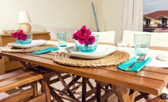 a wooden dining table set with blue glasses , plates , and a flower centerpiece , creating a casual and inviting atmosphere at Thetis