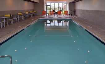 an indoor swimming pool with a large rectangular shape , surrounded by chairs and tables , and with a view of the outside at Home2 Suites by Hilton Merrillville