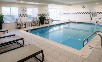 an indoor swimming pool surrounded by chairs and tables , with people enjoying their time in the pool area at Hilton Garden Inn Kennett Square