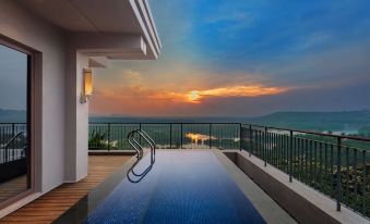 a modern , multi - level swimming pool with a glass railing and a stunning sunset view at sunset , captured from the perspective of the balcony at Hilton Goa Resort