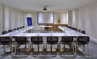 a large conference room with multiple tables , chairs , and a projector screen , set up for an event at Park Plaza Belvedere Medulin