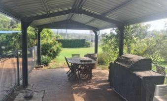 a patio with a table , chairs , and a grill under a covered area , surrounded by lush greenery at Valley View Motel