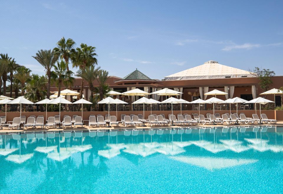 a large swimming pool with white umbrellas and lounge chairs in front of a building at Sol Oasis Marrakech - All Inclusive