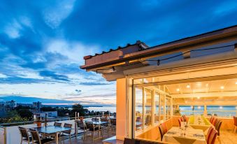 a rooftop dining area with tables and chairs , overlooking the ocean at dusk , under a beautiful blue sky at Best Western Hotel Rebstock