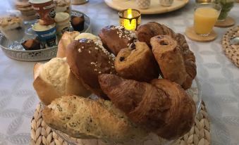 a variety of pastries and breads are displayed on a wicker tray , with candles and cups in the background at La Grenouillère