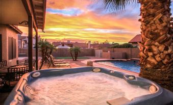 a backyard with a hot tub and a pool , surrounded by palm trees and a beautiful sunset at Arrowhead