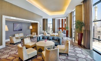 a modern living room with a large window , gray carpet , and various seating arrangements at Hilton Suites Makkah