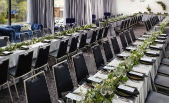 a long dining table with black chairs and white tablecloths is set up in a room with windows at Mantra Albury Hotel