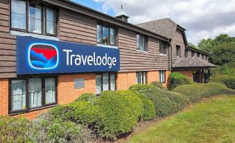 a travelodge hotel building with a blue and red sign on the side , surrounded by green grass and trees at Travelodge Ipswich Beacon Hill