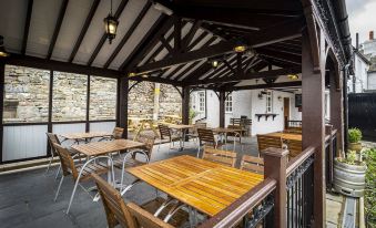 an outdoor dining area with wooden tables and chairs under a covered structure , surrounded by stone walls at Queens Head Inn