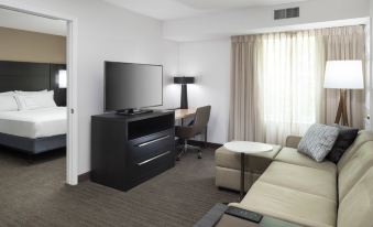 a modern hotel room with a large flat - screen tv , couch , and desk , along with curtains and wooden flooring at Residence Inn Boston Westford