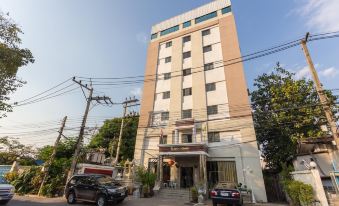 a tall building with a red door is surrounded by power lines and trees , with a car parked in front of it at Chaipat Hotel