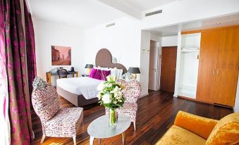 a spacious bedroom with a king - sized bed , two chairs , and a vase of flowers on the bedside table at The Ambassador
