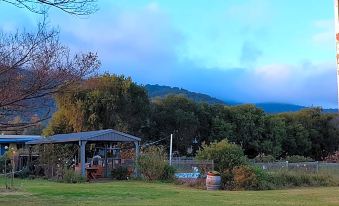 a grassy field with a small wooden structure in the middle , surrounded by trees and mountains in the background at Valley View Motel