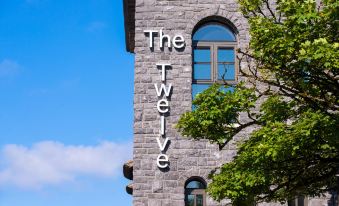 "a stone building with the words "" the twelve "" written on it , surrounded by trees and blue sky" at The Twelve Hotel