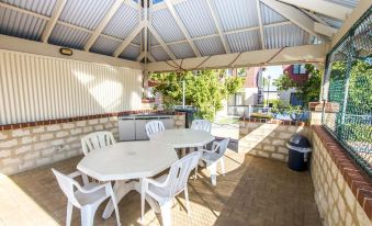 a patio with a white table and chairs under a corrugated metal roof , overlooking a swimming pool at Amalfi Resort