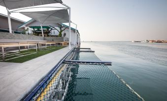 a swimming pool with a net and clear water , surrounded by green grass and white umbrellas at Baan Tah on the Sea