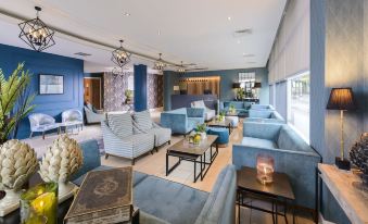 a spacious lounge area with blue sofas , a coffee table , and a chandelier , all arranged in a stylish setting at The Ellison