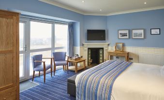 a hotel room with blue walls , a bed , and two chairs , along with a fireplace and a tv at Trearddur Bay Hotel