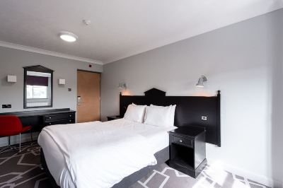 a large bed with white sheets and a black headboard is in a room with gray walls at Village Hotel Liverpool