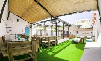 a green outdoor area with wooden furniture , umbrellas , and a dining table under a thatched roof at La Esperanza