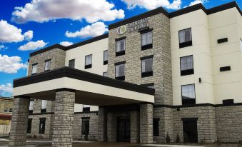 a large , modern hotel building with a red brick facade and a white roof under a blue sky at Cobblestone Hotel & Suites - Two Rivers