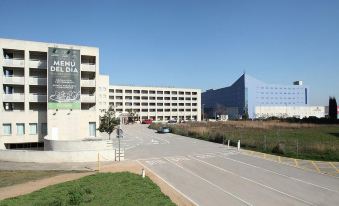 a large building with a green parking lot and cars parked in front of it at Travelodge Barcelona del Valles