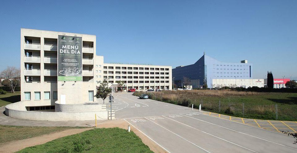 a large building with a green parking lot and cars parked in front of it at Campanile Barcelona