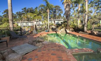 a large outdoor pool surrounded by palm trees , with lounge chairs and umbrellas placed around it at Fairway Motor Inn