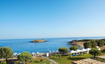 a beautiful coastal resort with clear blue skies , green trees , and umbrellas on the lawn at Grecotel Meli Palace