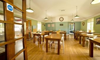 a room with wooden floors and tables , some of which have hanging lights and have green walls at YHA Malham