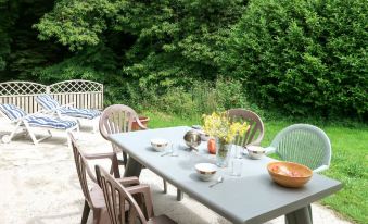 a patio table with chairs and a bowl of food is set up outside near a lush green forest at Entre Terre et Mer